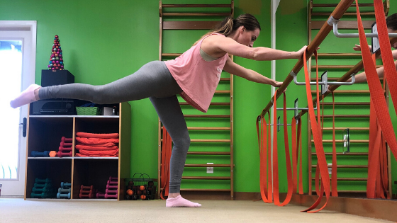 A woman demonstrates foldover with extension at the barre