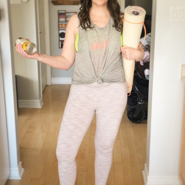 Woman holding a yoga mat and soup can in her kitchen.