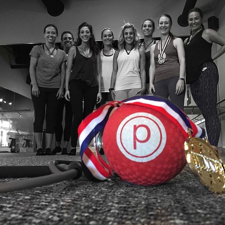 A medal is displayed on top of a red pure barre exercise ball while women stand in the background.