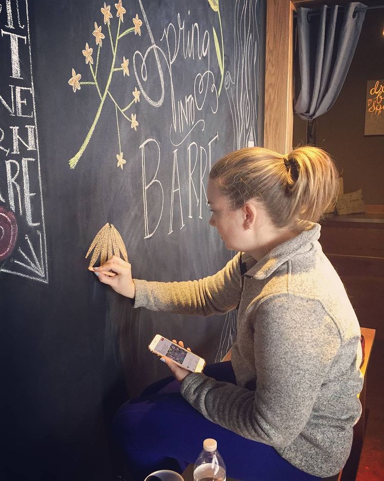 A woman creates an art piece on the chalkboard of Pure Barre McLean's location.